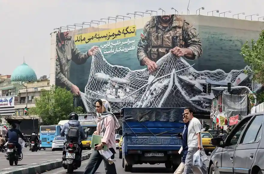 Iranian walks past a giant billboard reading 'The Strait of Hormuz remains closed' at Revolution Square in Tehran.