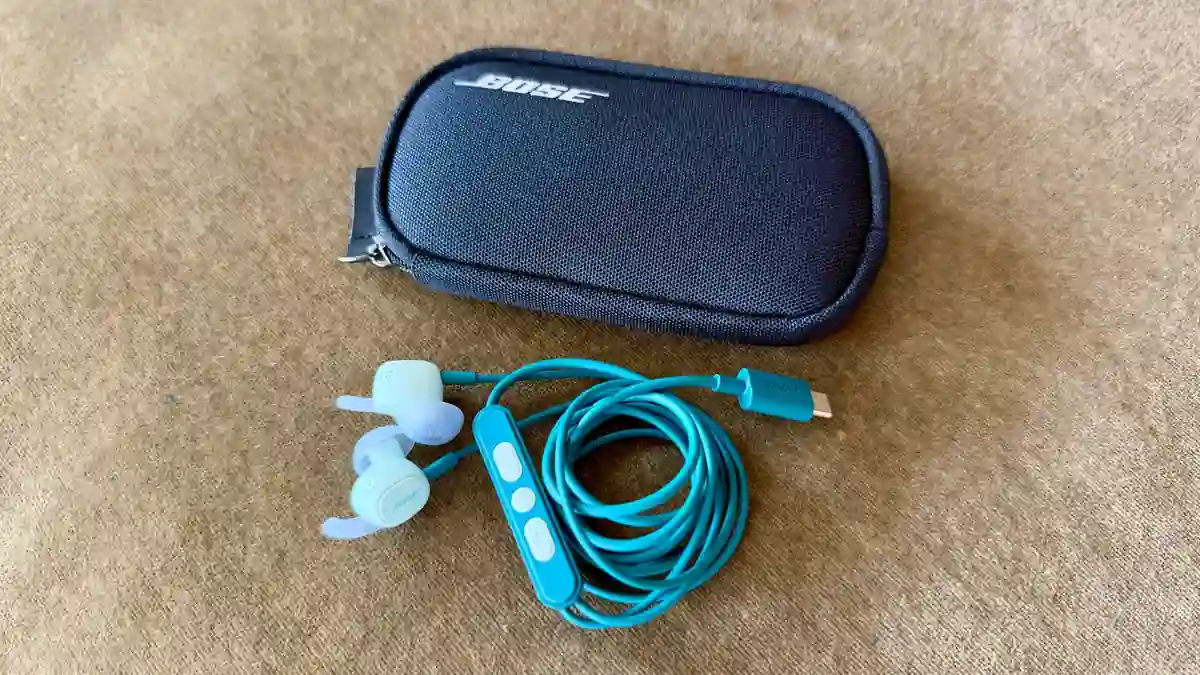 Bose wired earphones with an inline control microphone and carrying case placed on a fabric surface.