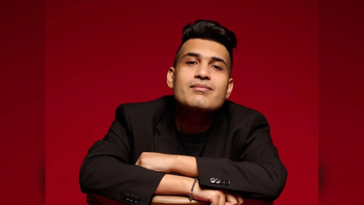 Music composer Shashwat Sachdev poses in a black suit against a red background.