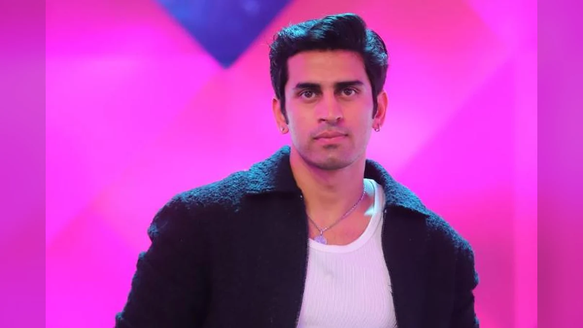 Bigg Boss 20 contestant Kushal Tanwar, popularly known as Gullu, poses in a black jacket and white shirt against a vibrant pink and purple background.