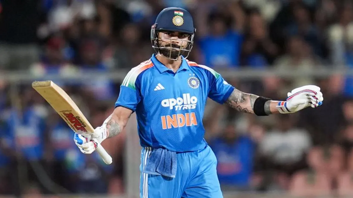 Virat Kohli celebrates after scoring for India in a cricket match, holding his bat and wearing the Indian cricket team jersey.